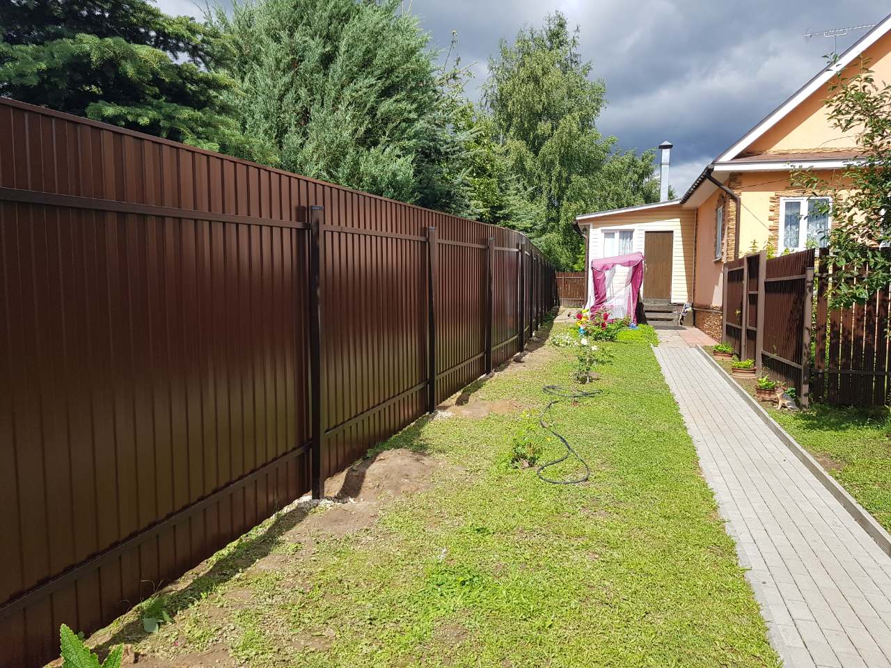 Дом с комбинированным забором и воротами на фоне заката